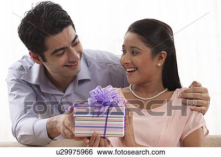 Stock Photograph - Handsome young man giving a gift to woman at home . Fotosearch