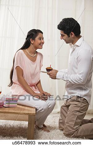 Stock Image - Handsome young man kneeling while giving cupcake to woman at home . Fotosearch