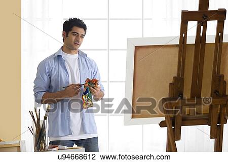 Stock Image - Handsome young man standing in front of easel in art studio . Fotosearch