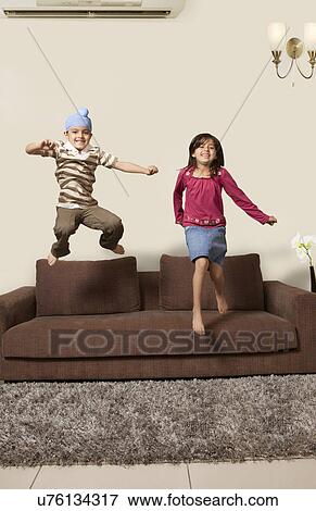 Happy brother and sister jumping on sofa at home View Large Photo Image Stock Photo - Happy brother and sister jumping on sofa at home . Fotosearch