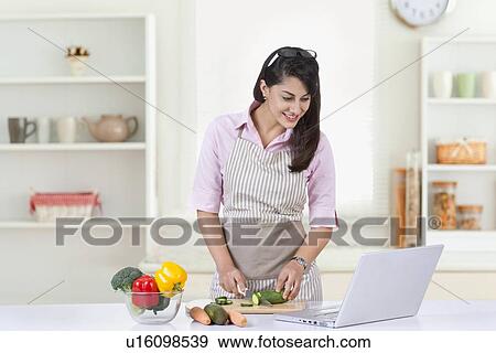Happy businesswoman looking at laptop while preparing food in kitchen View Large Photo Image Stock Photo - Happy businesswoman looking at laptop while preparing food in kitchen. Fotosearch
