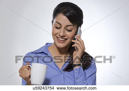 Happy businesswoman using phone while having coffee against gray background View Large Photo Image Picture - Happy businesswoman using phone while having coffee against gray background. Fotosearch