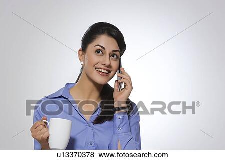 Stock Photo - Happy businesswoman with coffee mug answering phone over gray background. Fotosearch