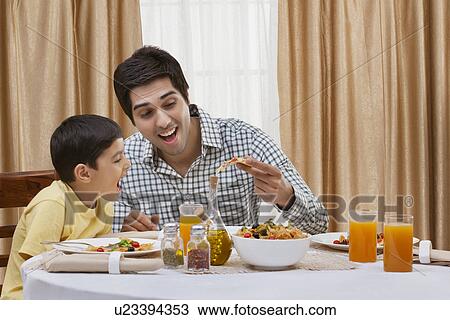 Stock Image - Happy father and son having pizza at restaurant . Fotosearch