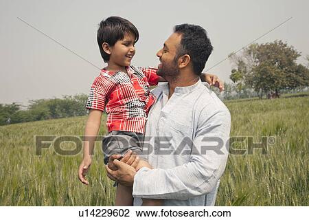 Stock Image - Happy father and son looking at each other with wheat field in background . Fotosearch