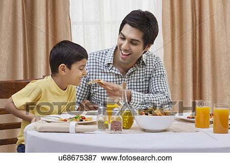 Happy father feeding piece of pizza to his son at restaurant View Large Photo Image Stock Photo - Happy father feeding piece of pizza to his son at restaurant . Fotosearch