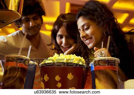 Stock Photography - Happy friends looking at popcorn and soft drink . Fotosearch
