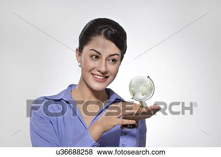 Happy Indian businesswoman looking at globe against gray background View Large Photo Image Stock Photo - Happy Indian businesswoman looking at globe against gray background. Fotosearch