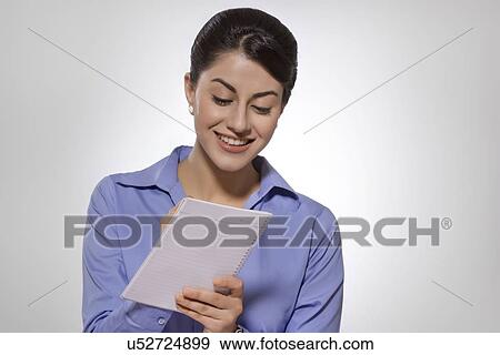 Happy Indian businesswoman writing on notebook against gray background View Large Photo Image Stock Photo - Happy Indian businesswoman writing on notebook against gray background. Fotosearch
