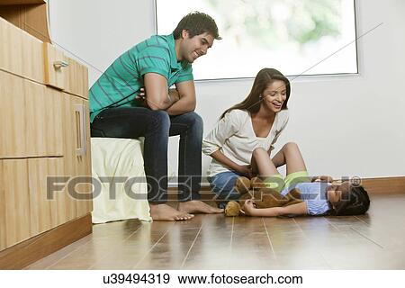 Stock Photo - Happy mother playing with daughter while father sitting besides . Fotosearch