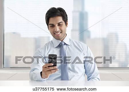 Happy young businessman texting message through cell phone View Large Photo Image Stock Photography - Happy young businessman texting message through cell phone . Fotosearch
