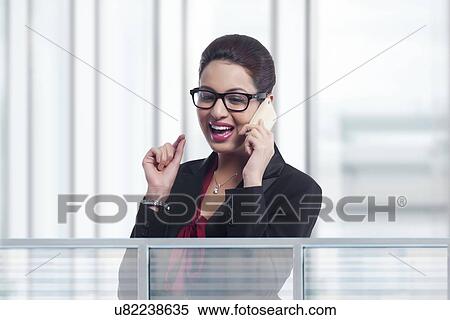Happy young businesswoman answering mobile phone in office View Large Photo Image Stock Photography - Happy young businesswoman answering mobile phone in office. Fotosearch