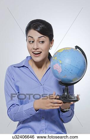 Happy young businesswoman looking at globe against gray background View Large Photo Image Stock Photograph - Happy young businesswoman looking at globe against gray background. Fotosearch