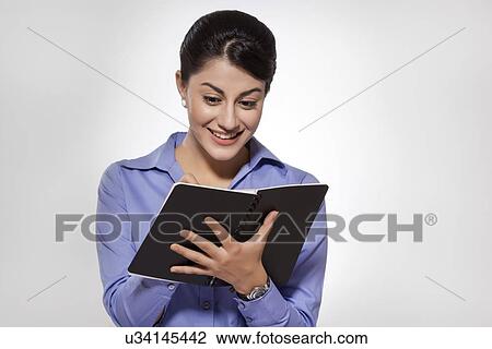 Stock Image - Happy young businesswoman writing on note pad against gray background. Fotosearch
