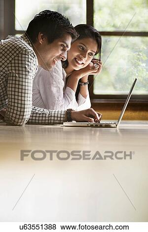 Happy young couple lying on floor with laptop View Large Photo Image Stock Photo - Happy young couple lying on floor with laptop . Fotosearch