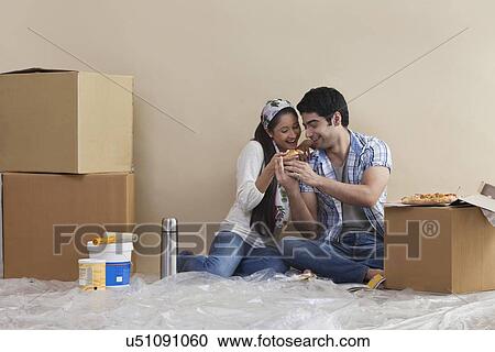 Stock Image - Happy young couple sharing pizza at their new home . Fotosearch