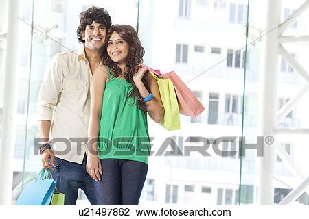 Stock Image - Happy young couple smiling while holding shopping bags together . Fotosearch