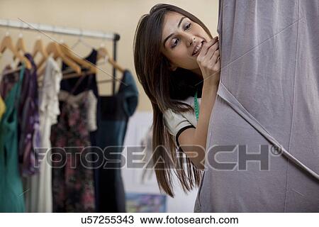 Stock Image - Happy young female designer fixing dress on mannequin in studio . Fotosearch