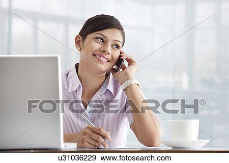Stock Photo - Happy young female executive using cell phone at her desk . Fotosearch