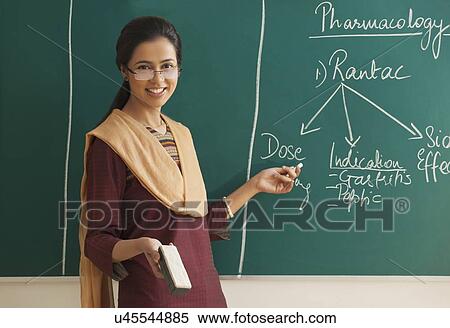 Stock Photography - Happy young female teacher holding duster and chalk against green board . Fotosearch