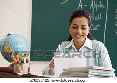 Happy young female teacher reading document at desk View Large Photo Image Stock Photography - Happy young female teacher reading document at desk . Fotosearch