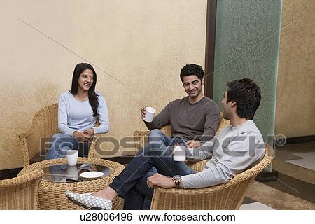 Happy young friends having coffee together while sitting on wicker chair at home View Large Photo Image Stock Photograph - Happy young friends having coffee together while sitting on wicker chair at home . Fotosearch