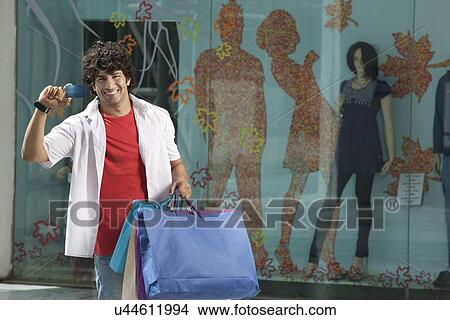Picture - Happy young man showing his credit card at shopping mall . Fotosearch