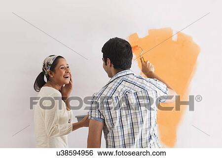 Happy young woman looking at man while painting wall View Large Photo Image Stock Photograph - Happy young woman looking at man while painting wall . Fotosearch