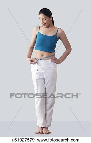 Stock Photo - Happy young woman measuring waist against gray background . Fotosearch