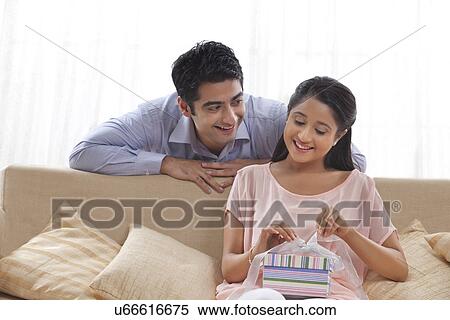 Stock Photography - Happy young woman unwrapping present gifted by man . Fotosearch