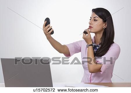 Indian businesswoman applying lipstick at office desk View Large Photo Image Stock Image - Indian businesswoman applying lipstick at office desk. Fotosearch