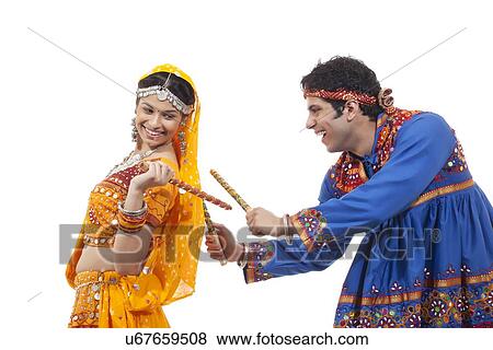 Indian couple in traditional wear performing Dandiya Raas over white background View Large Photo Image Stock Photo - Indian couple in traditional wear performing Dandiya Raas over white background. Fotosearch