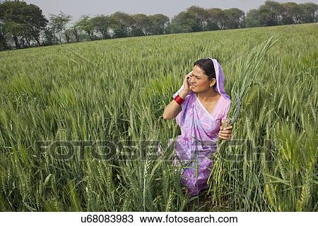 Stock Image - Indian female farm worker talking on cell phone while working in field . Fotosearch