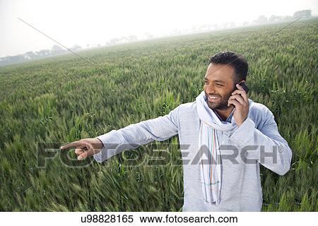 Indian man in a field pointing away while on a call View Large Photo Image Stock Photography - Indian man in a field pointing away while on a call . Fotosearch