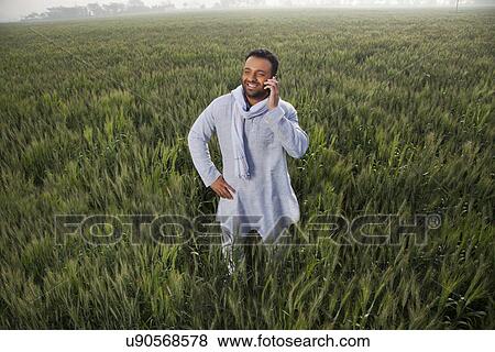 Stock Photo - Indian man in a field talking on phone with hand on hip . Fotosearch