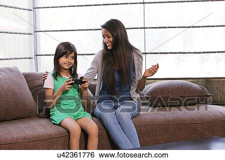 Stock Photograph - Little girl playing video game while mother looking at her . Fotosearch