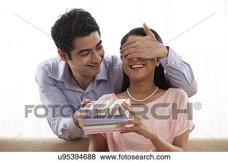 Loving man giving a surprise gift to woman at home View Large Photo Image Stock Photo - Loving man giving a surprise gift to woman at home . Fotosearch