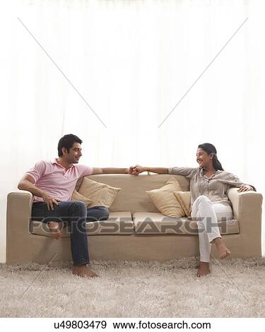 Stock Photo - Loving young couple holding hands while sitting on sofa . Fotosearch