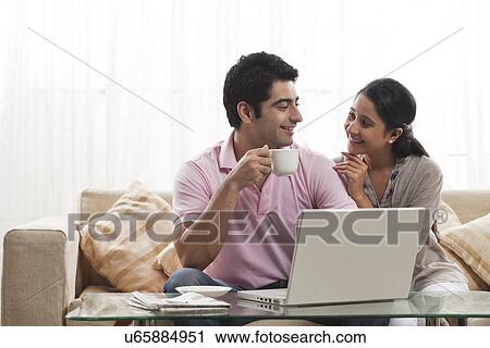 Stock Image - Loving young man looking at woman while holding coffee cup with laptop . Fotosearch