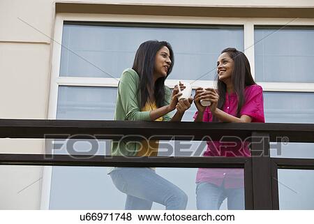 Low angle view of female friends looking at each other while having coffee in balcony View Large Photo Image Stock Photo - Low angle view of female friends looking at each other while having coffee in balcony . Fotosearch