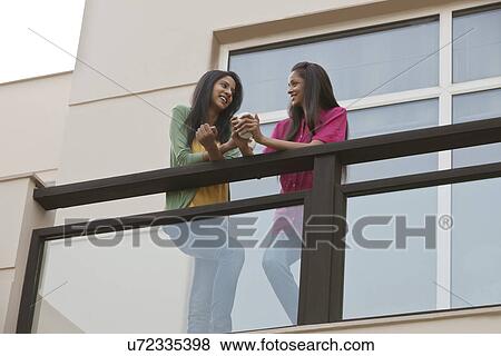 Low angle view of female friends standing together while having coffee in balcony View Large Photo Image Stock Photo - Low angle view of female friends standing together while having coffee in balcony . Fotosearch