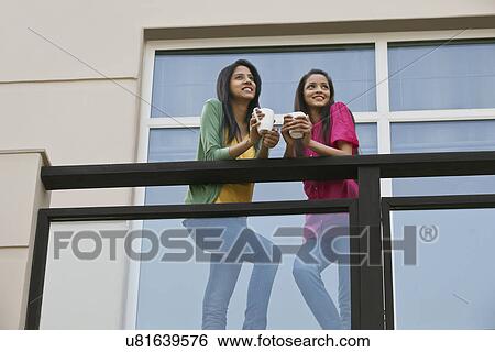 Low angle view of young female friends looking away while having coffee in balcony View Large Photo Image Stock Photograph - Low angle view of young female friends looking away while having coffee in balcony . Fotosearch