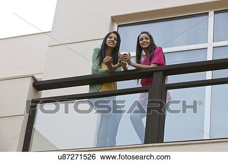Low angle view of young female friends looking away while having coffee in balcony View Large Photo Image Stock Photograph - Low angle view of young female friends looking away while having coffee in balcony . Fotosearch
