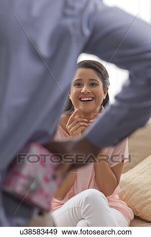 Man hiding surprise gift from happy woman View Large Photo Image Stock Photo - Man hiding surprise gift from happy woman . Fotosearch