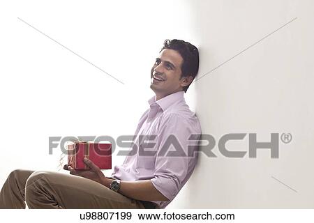 Man holding a gift leaning against wall View Large Photo Image Stock Photo - Man holding a gift leaning against wall. Fotosearch