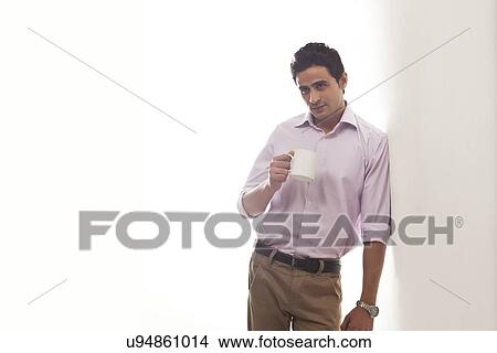 Man holding a mug of tea leaning against wall View Large Photo Image Picture - Man holding a mug of tea leaning against wall. Fotosearch