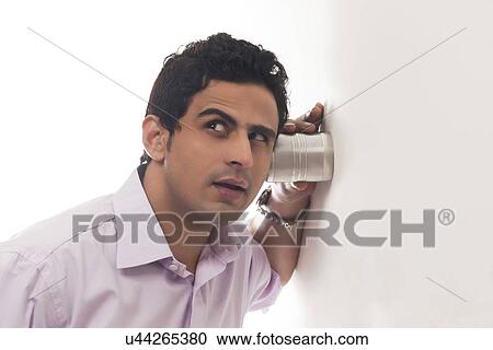 Stock Image - Man holding glass against wall listening. Fotosearch