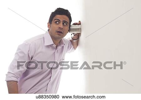 Stock Image - Man holding glass against wall listening. Fotosearch