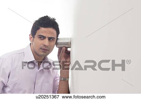 Stock Photo - Man holding glass against wall listening. Fotosearch