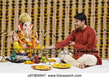 Stock Photo - Man offering flowers to Lord Ganesh . Fotosearch